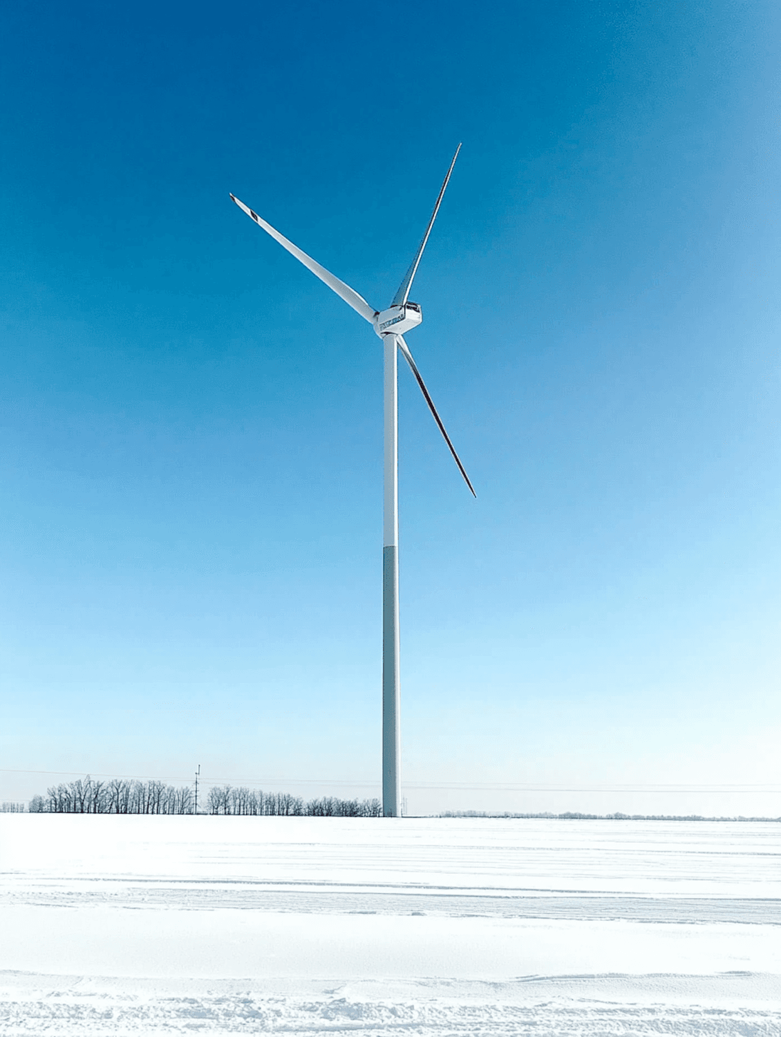 A single white wind turbine standing in a snowy field under a clear blue sky