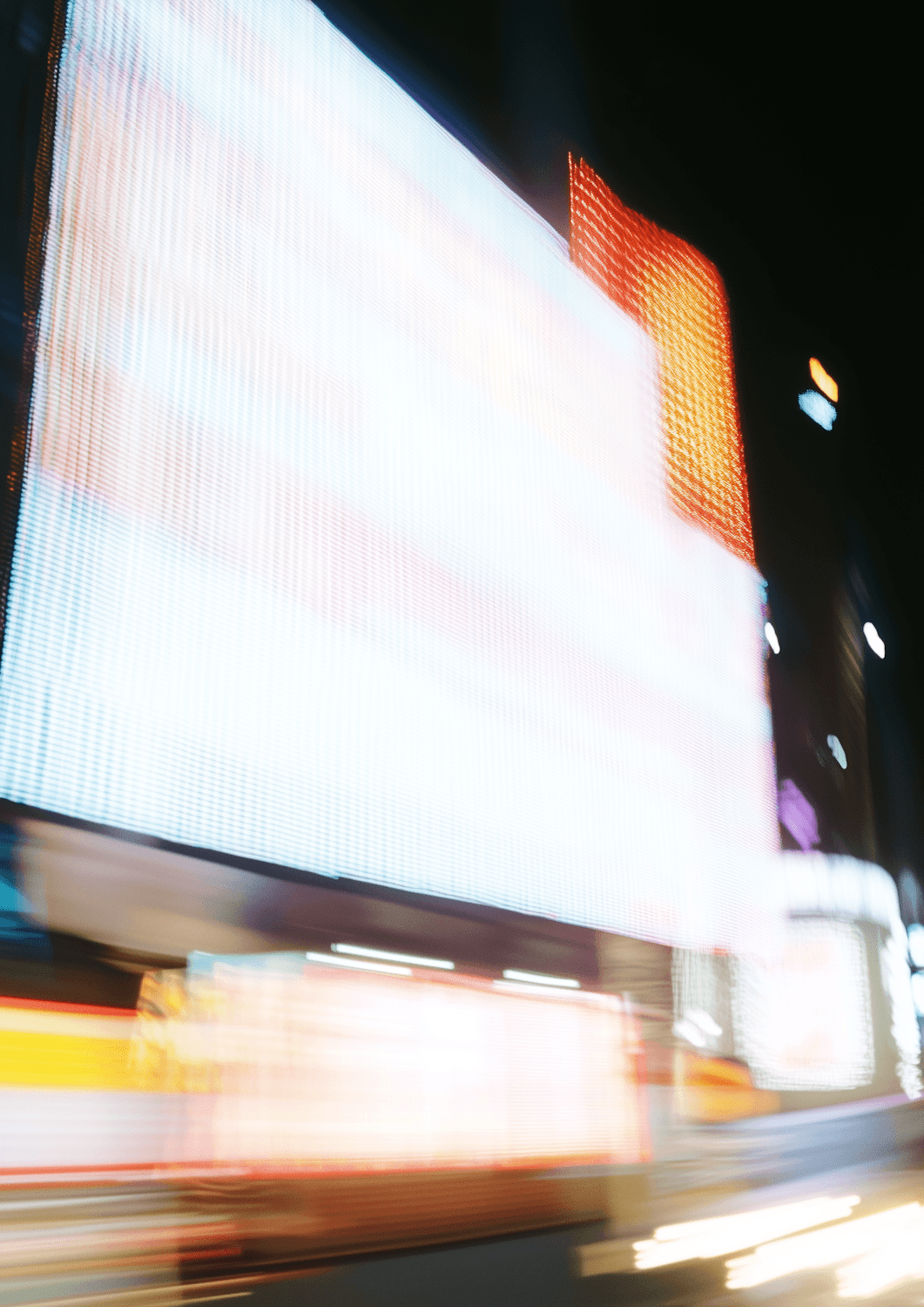 A giant glowing digital billboard blurred by motion on a city street at night
