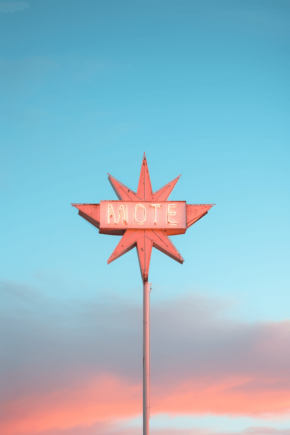 A retro neon starburst sign glowing pink against a blue evening sky